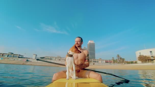 Мужчина и милая собака на солнечном пляже день на доске для серфинга — стоковое видео