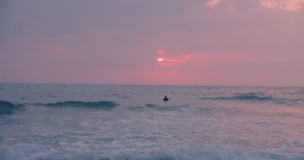 穿着雨衣在日落海滩冲浪的年轻人 — 图库视频影像