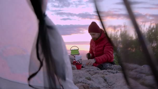 El hombre hace café al acampar al atardecer — Vídeo de stock