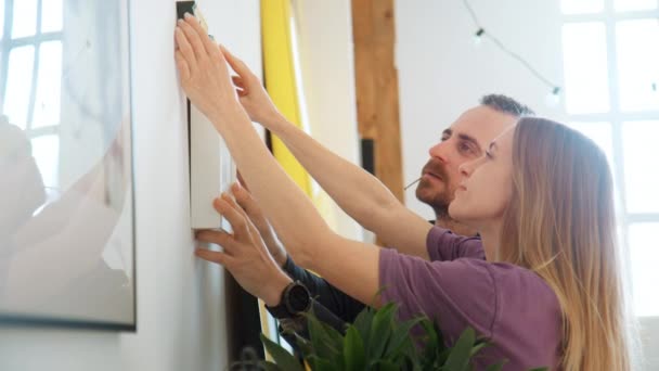 Δημιουργικό ζευγάρι κρέμεται ζωγραφική σε μοντέρνο διαμέρισμα — Αρχείο Βίντεο