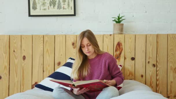 Ung söt student studerar fjärr för bok i sängen — Stockvideo