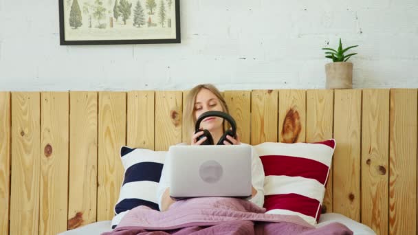 Fiatal nő fülhallgatóval és laptoppal az ágyban — Stock videók