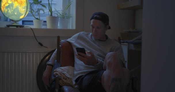 Casual jonge man ontspannen op fauteuil met telefoon — Stockvideo