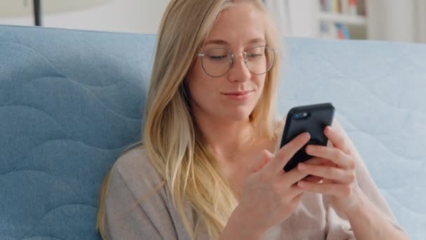Νεαρή όμορφη γυναίκα χρησιμοποιούν smartphone στον καναπέ στο σπίτι — Αρχείο Βίντεο