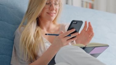 Genç ve güzel bir bayan evdeki koltukta akıllı telefon kullanıyor.