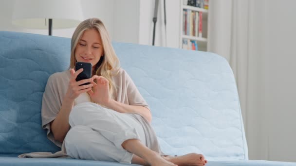 Jovem mulher bonita usar smartphone no sofá em casa — Vídeo de Stock