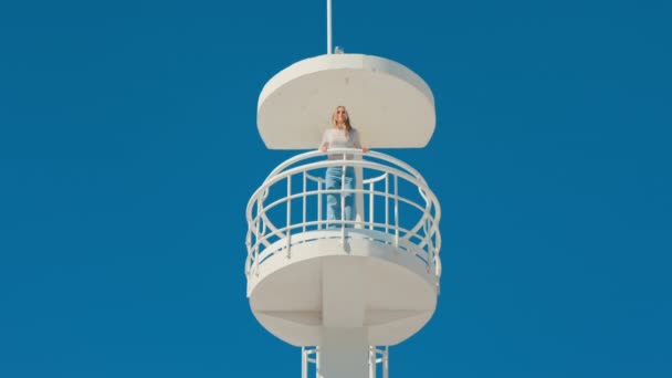 Meisje in strandwacht toren op geïsoleerde blauwe lucht — Stockvideo