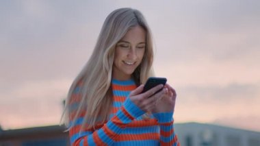 Genç milenyum kadını günbatımında akıllı telefon kullanır.