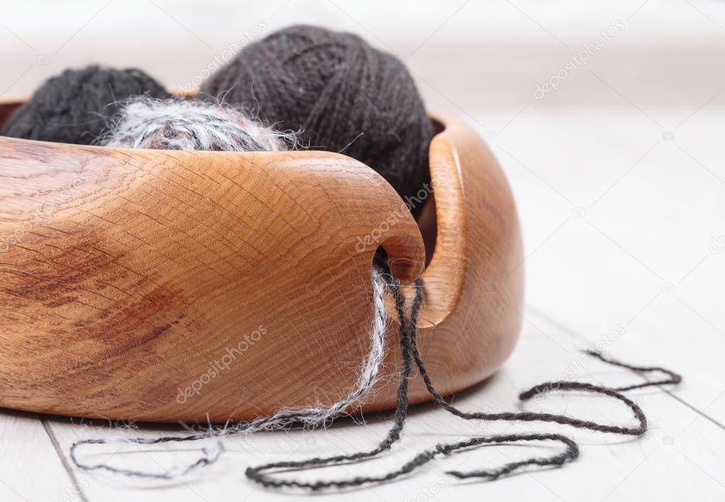 knitting with a wool yarn ball in a wooden bowl on a white oak d