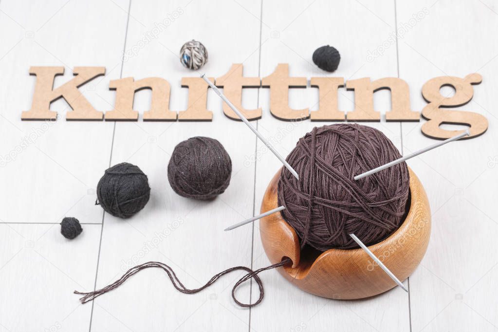 knitting with a wool yarn ball in a wooden bowl on a white oak d