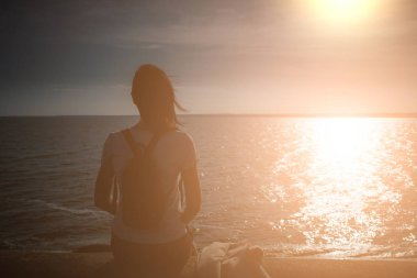 Kız sahil deniz taş dolgu üzerinde oturur ve bakar 