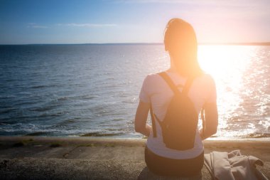 Kız sahil deniz taş dolgu üzerinde oturur ve bakar 