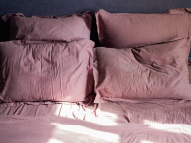 Dört buruşuk yastık ve yatağın üzerinde bir çarşaf ve güneş üstlerinde parlıyor.