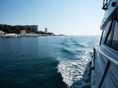 Teknenin sağ tarafında, denizin arka planında.