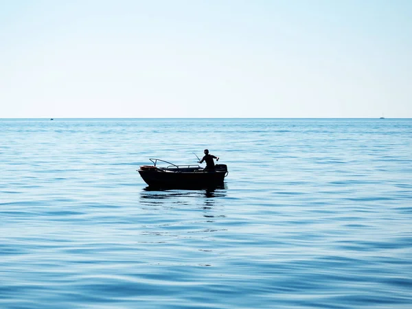 Silhueta de um pescador em um barco lança uma vara de pesca no mar — Fotografia de Stock