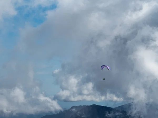 Ein Mann fliegt mit einem Gleitschirm über die Berge vor blauem Himmel und Wolkendunst — Stockfoto