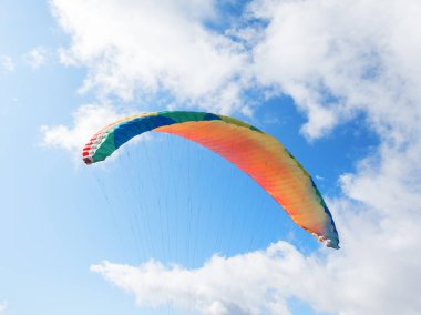 Mavi gökyüzüne ve bulutlara yaslanmış paraglider kubbesi.