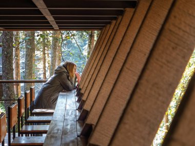 Gri ceketli, kapüşonlu bir kız bir orman kafesinde bir barda oturuyor.