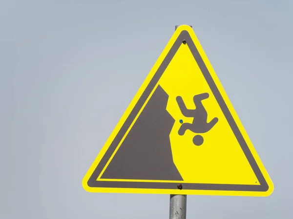Желтый треугольный знак с человеком, падающим со скалы на сером фоне — стоковое фото