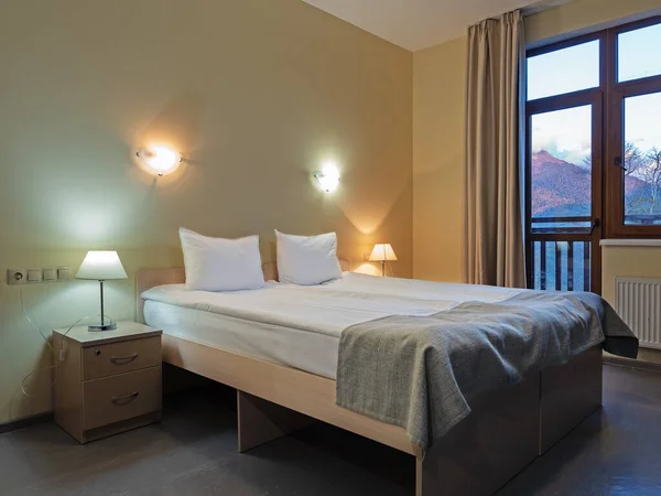 Room with a double bed with table and wall lights and a mountain view from the window