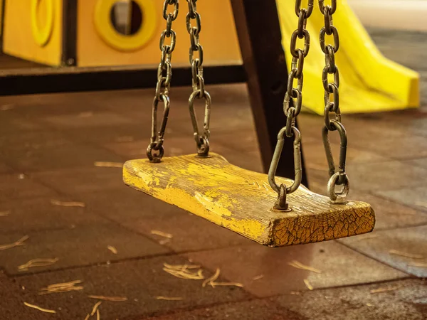 Närbild foto av en gunga på metallkedjor med en gul träsits på bakgrunden av lekplatsen — Stockfoto