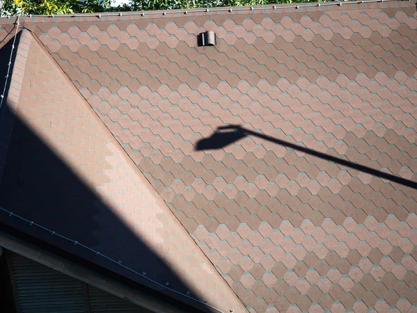 Una foto de cerca del techo marrón de la casa con azulejos y una sombra de un poste de luz en ella — Foto de Stock
