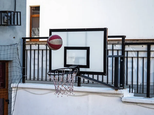 Baloncesto rojo-blanco volando en una red conectada a una valla negra metálica — Foto de Stock