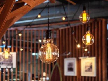 Decorative glowing light bulbs hanging in the interior of the cafe against the background of paintings hanging on wooden partitions