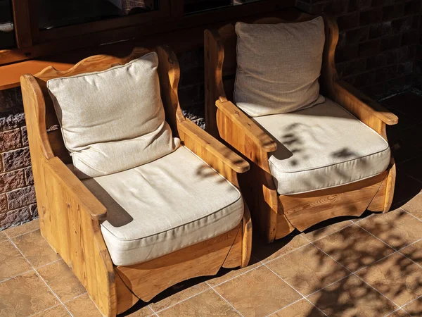 Two wooden chairs with soft fabric sydles stand on the tiled floor, illuminated by the sun — 스톡 사진