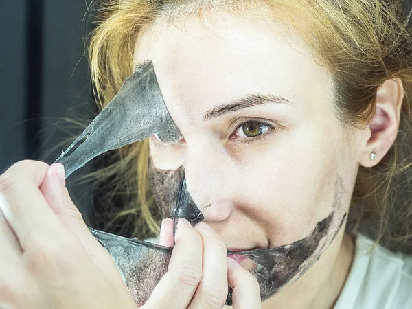 Девушка осторожно снимает с лица черную тонкую прозрачную маску для очистки пор — стоковое фото