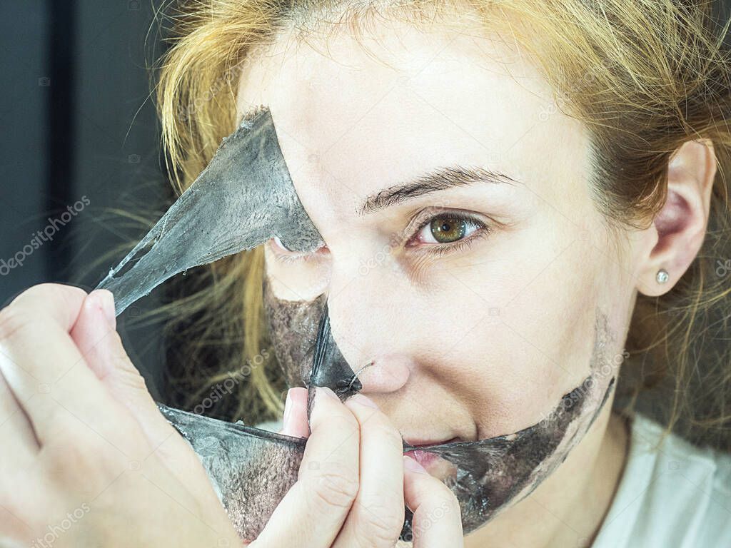 The girl carefully removes from her face a black thin transparent mask for cleaning pores