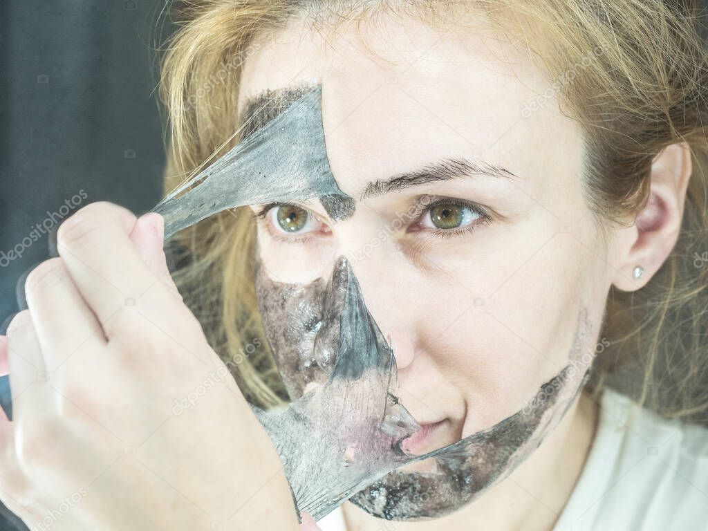 Blonde girl takes off from the face black thin transparent mask to clean pores