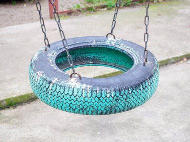 Mavi boyayla boyanmış ve zincirlenmiş bir araba tekerleğinden bir koltukla sallan.