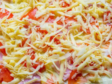 Hamurun üzerine konmuş domates ve jambon şeklinde pişirme hazırlığı rendelenmiş peynir serpiştirildi.