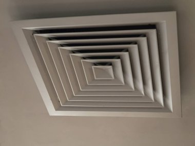 Photo at an angle of a ventilation hatch with a cover with a square pattern hanging on a light ceiling clipart