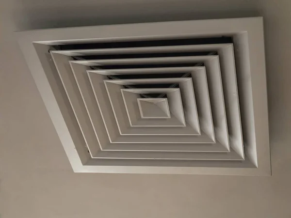 Фото под углом вентиляционного люка с крышкой с квадратным рисунком, висящим на светлом потолке — стоковое фото