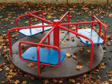 Oyun alanında sarı yapraklarla kaplı yuvarlak salıncak.