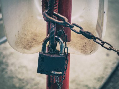Paslı asma kilit zincirli kırmızı bir boruda asılı.