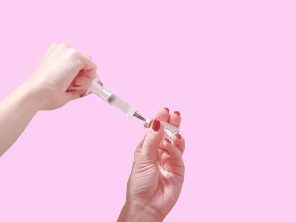 Een hand met rode nagels houdt een spuit vast. Het meisje houdt een spuit voor puntig vast. Geneeskunde. Roze achtergrond, plaats voor tekst. — Stockfoto