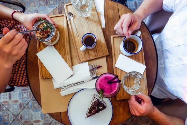 Paar von Mann und Frau auf Date beim Frühstück am Morgen im Café. Müsli, Schokoladenkuchen, Smoothie und heißer Kaffee auf dem Tisch. Flatlay, selektiver Fokus. — Stockfoto