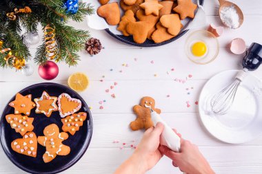 Kadın bir mutfak beze krema ile gingerbread adam çerezleri dekorasyon inprocess ihale eller. İngrediens ve dekorasyon ayrıntıları ile beyaz ahşap masa. Noel arka plan kavramı.
