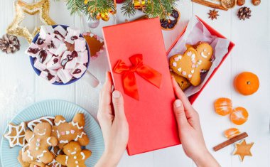 Üstten Görünüm kadın el yapımı geleneksel Noel zencefilli kurabiye adam kurabiye ile kırmızı hediye kutusundan kapak tutan eller. Beyaz ahşap masa dekorasyonu ile. Noel kavramı. Seçici odak.