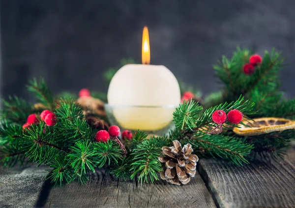 Cristmas card with focused fir cone and branches of advent wreath with natural decor and blurred burning candle on the old rustic table with dark stone background. Selective focus. Space for text. — Stock Photo, Image