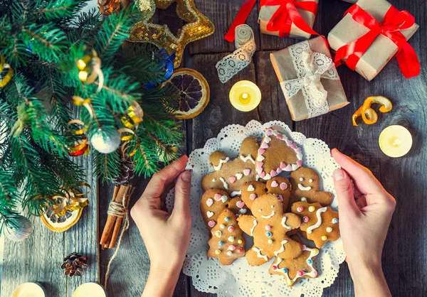 Widok z góry kobieta ręce, trzymając płytkę z domu pierniki na starych rustykalnych drewniany stół z gałęzi jodły, zabawki, ozdoba, sosna stożek, pudełeczka, świece. Tło vintage Christmas, — Zdjęcie stockowe