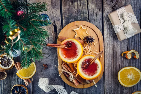 Noel mulled şarap - alışılmadık turuncu görev yaptı. Çilek, portakal, baharatlar, hediyeler, çam dalları, dekor, eski ahşap tablo tarçın içkiyle sıcak kış mumlar. Vintage kartı, seçici odak