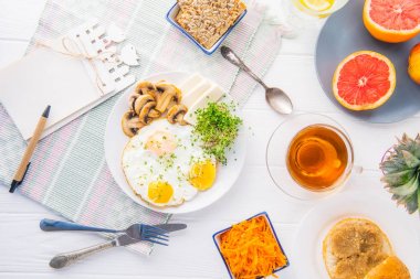 Defter ile emty boşluklar ve sağlıklı kahvaltı tabağı pişmiş yumurta, peynir, kızarmış mantar ve Filiz mikro Yeşiller hizmet beyaz tahta masada. Üstten Görünüm. Seçici odak.