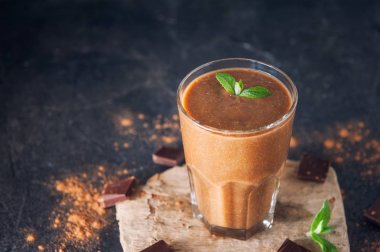 Muz, çikolata yüzlü adet çikolata ve kakao tozu ile koyu arka plan üzerine nane yaprağı ile dekore edilmiştir. Sağlıklı bir diyet yemek. Seçici odak, metin için yer.