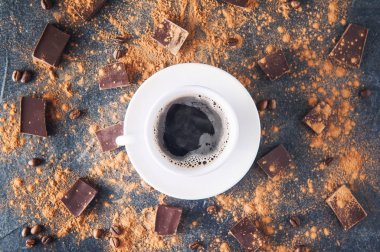 Fasulye, kakao tozu ve çikolata parçaları karanlık bir taş zemin üzerine siyah kahve fincan üstten görünüm dağılmış. Seçici odak. Metin için yer.