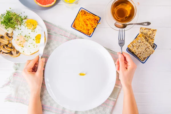 Top view female hands holding knife and fork and white plate with vitamin pill on the served wooden table with breakfast meal. Pill instead of food. Healthy diet concept. Selective focus. — Stock Photo, Image