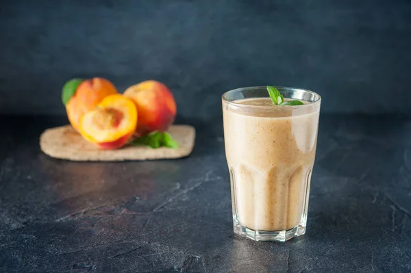 Bicchiere di frullato di frutta di pesca con foglie di menta e ingridienti sullo sfondo scuro. Alimentazione sana, vegetariana, vegana. Focus selettivo, spazio per il testo . — Foto Stock